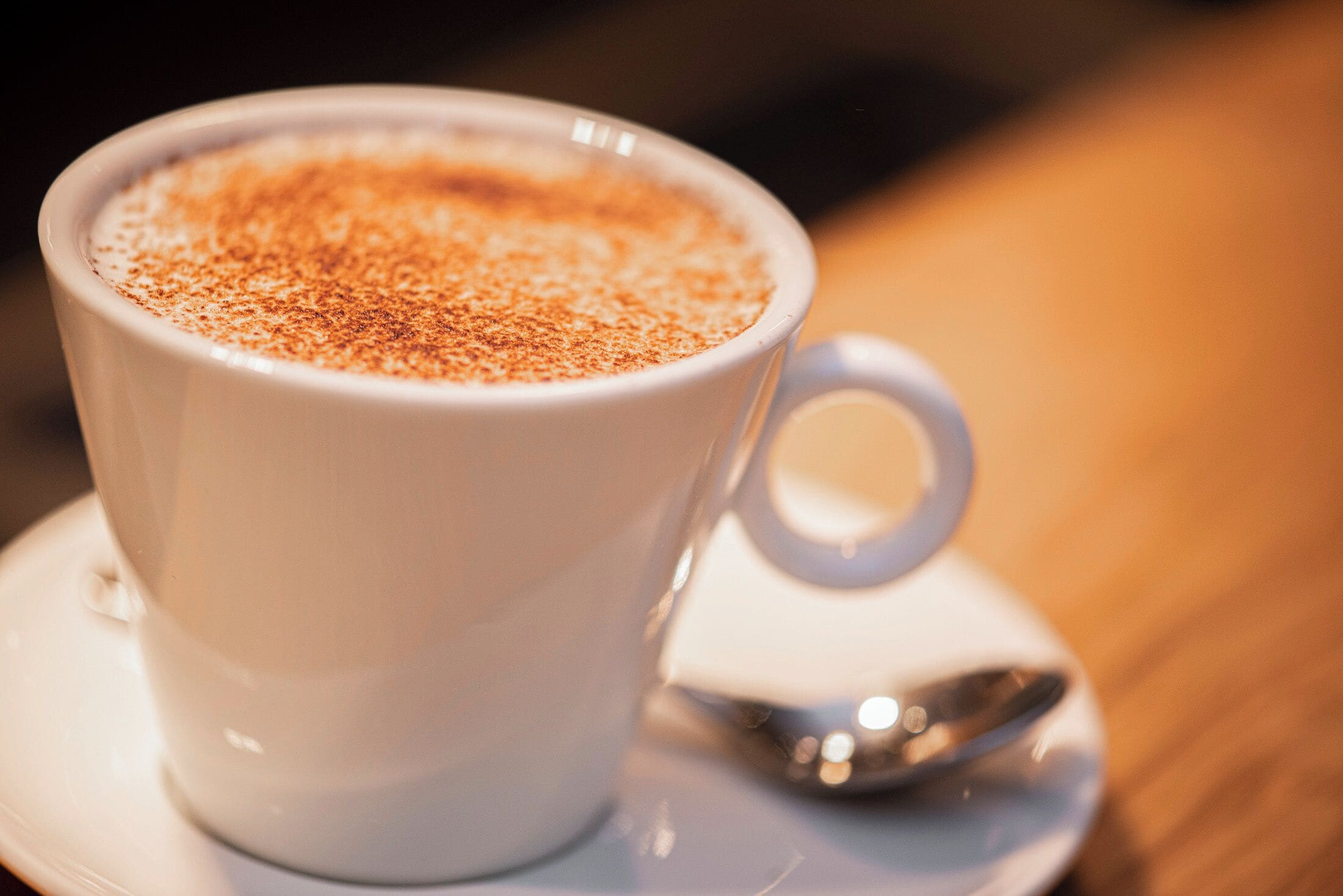 A white cup of coffee with a saucer and spoon on a table.