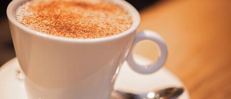A white cup of coffee with a saucer and spoon on a table.