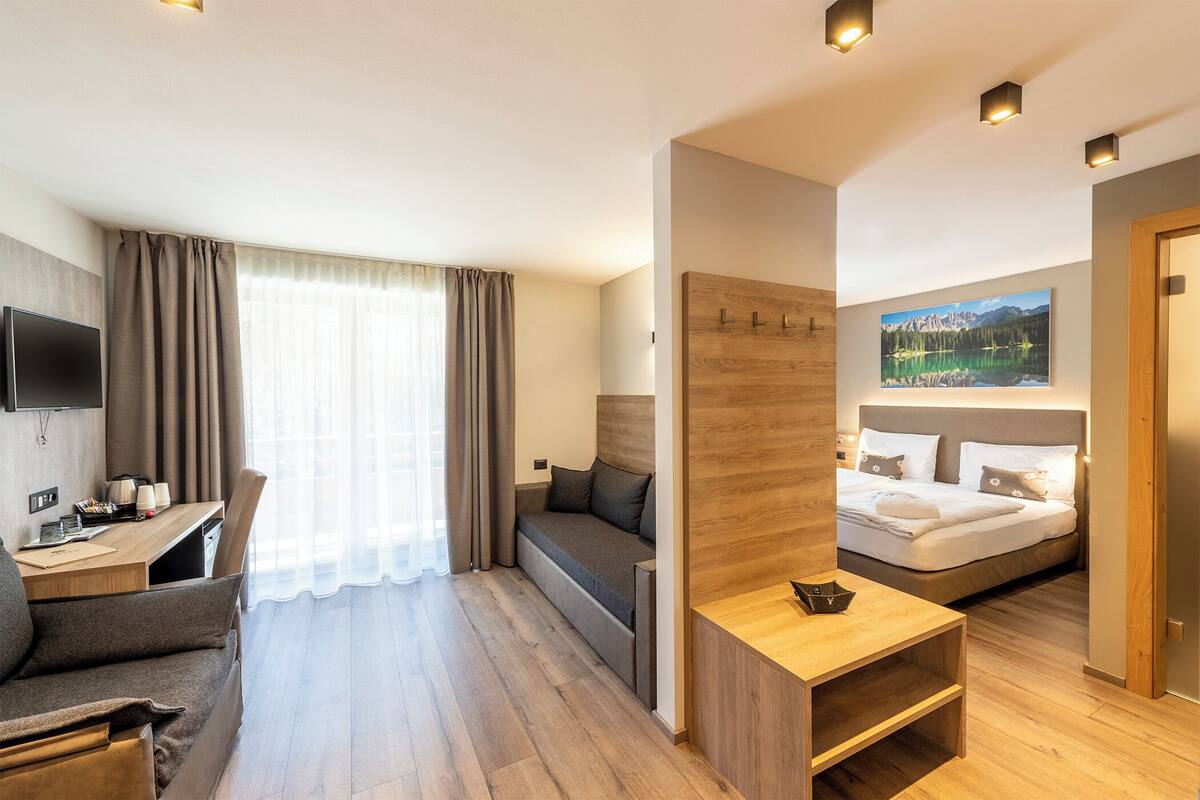 A modern hotel room with a sofa, a desk, a bed, and a TV.