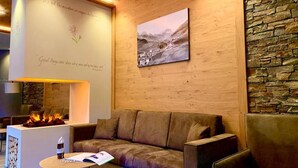 A cozy lounge area with a fireplace, a stone wall, and a painting of a mountainous landscape. - Chalet Aster (Moena)