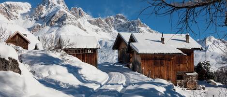 Una cabaña de madera con techo nevado, rodeada de un paisaje montañoso cubierto de nieve.