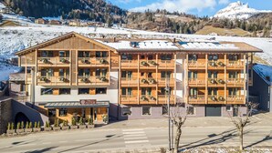 A multi-story wooden building with balconies, a sign reading "ASTER," and a view of a snowy mountain range. - Chalet Aster (Moena)
