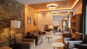 A modern lounge area with a stone wall, leather sofas, and a wooden ceiling. - Chalet Aster (Moena)