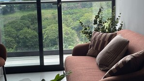A modern living room with a large window offering a view of a lush green landscape. - Luxury Stay in Nucleo Sabana, AC, WIFI, Pools, Parking and 30 more amenities (San José)