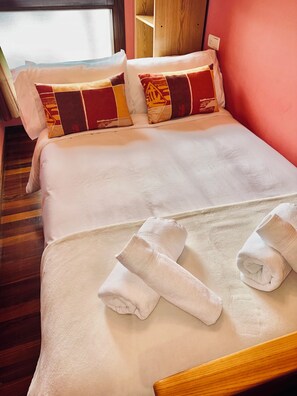 A hotel room with two beds, each with a white bedspread and patterned pillows. There are two rolled towels on the bed.