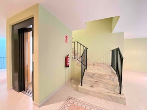 Un hall d’hôtel avec un escalier en marbre, un extincteur et une porte donnant sur une autre pièce.