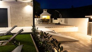 Eine moderne Terrassenanlage mit Grill, Sitzgelegenheit und gepflegtem Rasen.