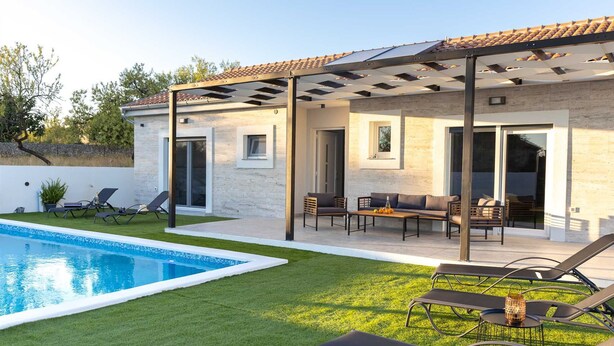 Ein modernes Haus mit Schwimmbad, Außenbereich mit Sitzgelegenheiten und einer überdachten Terrasse.