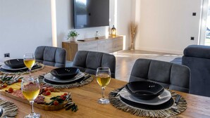 Ein Essbereich mit einem Holztisch, gedeckt für vier Personen, wobei jeder Platz einen schwarzen Teller und ein Glas Weißwein hat.