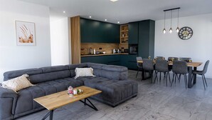 Ein modernes Wohnzimmer mit einem grauen Ecksofa, einem Holztisch und einem Essbereich mit Tisch und Stühlen.