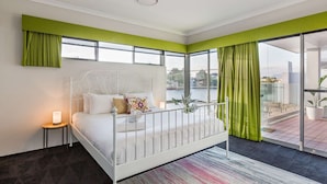 Ein modernes Schlafzimmer mit einem weißen Bett, grünen Vorhängen und Blick auf eine Stadtlandschaft durch große Fenster.