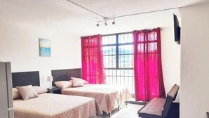 A hotel room with two beds, a desk, and a window with red curtains.