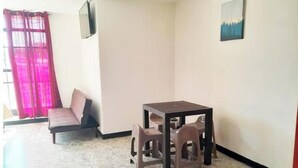 A small room with a single table and two chairs, a sofa, a window with pink curtains, and a painting on the wall.