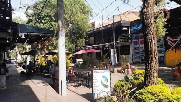 An outdoor cafe with tables and chairs, surrounded by greenery and a building with a sign. - 2 Nice and comfortable central apartment (Ciudad de Guatemala)