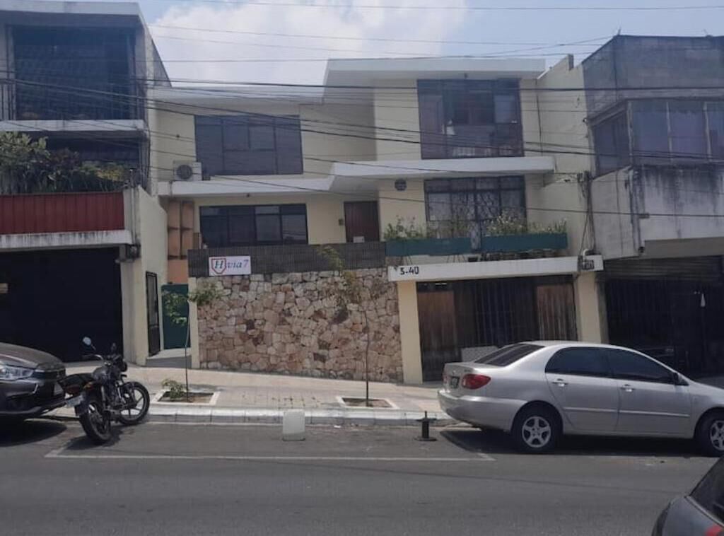 A multi-story building with a stone facade, a balcony with plants, and a sign indicating a price of 5.40.