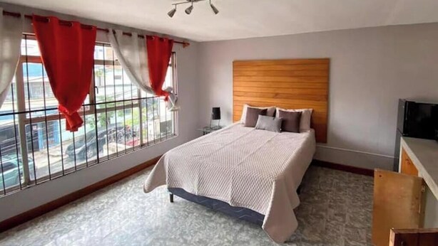 A bedroom with a bed, a wooden headboard, a television, and a window with red curtains. - 4 Stunning Cool Studio in tourist area (Ciudad de Guatemala)