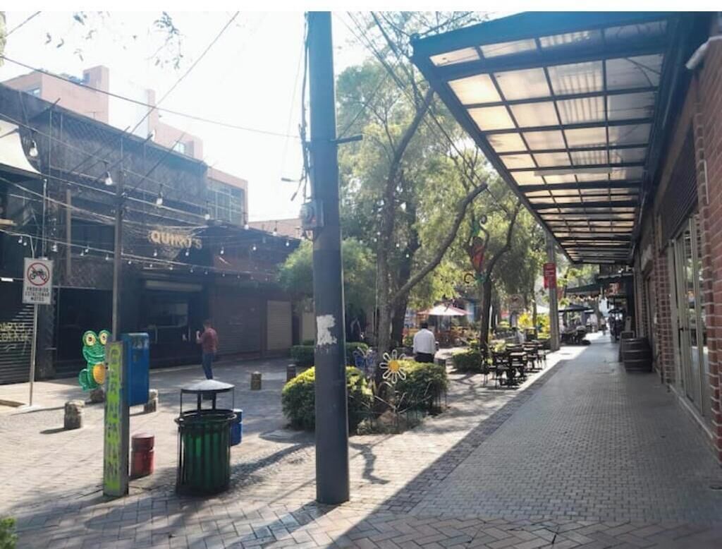 Una calle peatonal con mesas al aire libre, una zona cubierta y un edificio con un cartel.