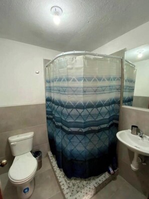 Un baño con cortina de ducha, inodoro, lavabo y suelo de baldosas.