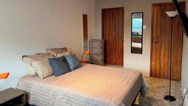 Un dormitorio con cama, armario, espejo y lámpara de pie.