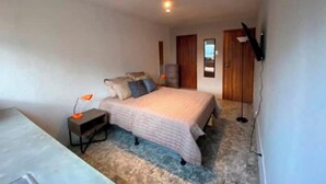 Un dormitorio con cama, mesita de noche, lámpara y televisor montado en la pared.