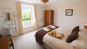 A hotel room with a bed, a bedside table, a window with curtains, a wooden wardrobe, a bathroom with a sink, and a radiator. - Old Belfield, Bowness-on-Windermere with lake view (Bowness-on-Windermere)