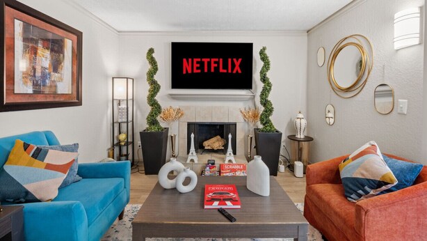 A modern living room with a fireplace, two sofas, a coffee table with a book, and a TV displaying 'NETFLIX'. - 2 Lux King Beds - Short Walk to Truist Park (Smyrna)