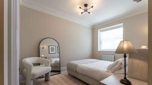 Een slaapkamer met een bed, een stoel, een nachtkastje met een lamp, een spiegel en een raam.