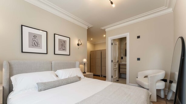 Een slaapkamer met een groot bed, een nachtkastje, een stoel en een kledingkast.