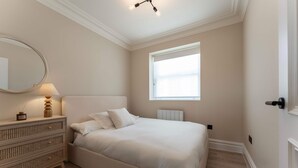 Een slaapkamer met een bed, een dressoir, een spiegel en een raam.