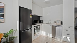 A modern kitchen with white cabinetry, a black refrigerator, a microwave, and a dishwasher. - Morepork Retreat - 1BDRM & Central (Queenstown)