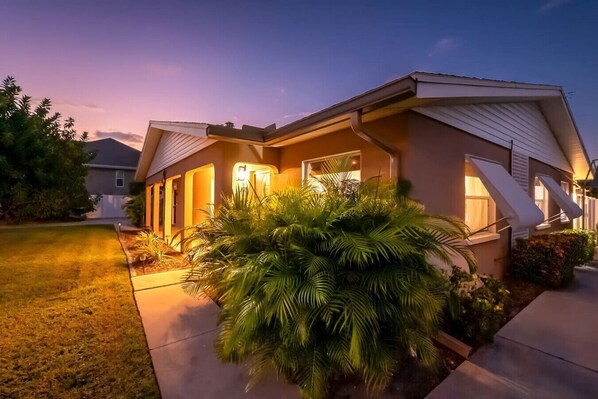 A modern two-story house with a well-lit front yard and a large palm tree.