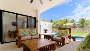 A sunlit patio with wooden furniture, a pool, and a view of a lush landscape. - Charming 3-bedroom villa in wonderful Ocean Village with Pool & BBQ (Sosúa - Caberete)