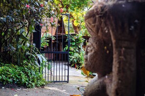 A garden with a metal gate, lush greenery, and a stone statue. - Linear Carpenter House (Cobano)