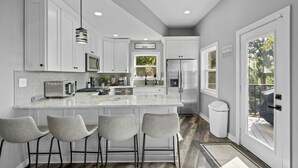 A modern kitchen with white cabinets, a central island with bar stools, a microwave, and a refrigerator.