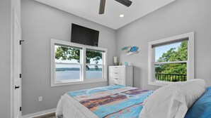 A bedroom with a large bed, two windows, a TV, and a view of the outdoors.