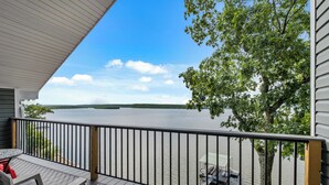 A wooden deck with a metal railing overlooking a lake, a table with chairs, and a covered area with a table and chairs.