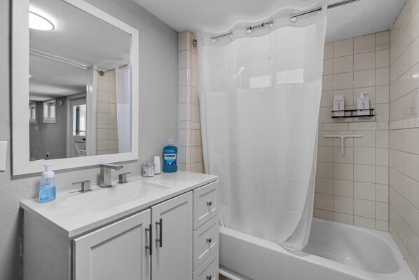 A bathroom with a white sink, mirror, and bathtub. There are toiletries on the sink and a shower curtain.