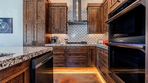 A kitchen with wooden cabinets, a stainless steel range hood, a microwave, and a dishwasher. - Village Camp Moab (Moab)