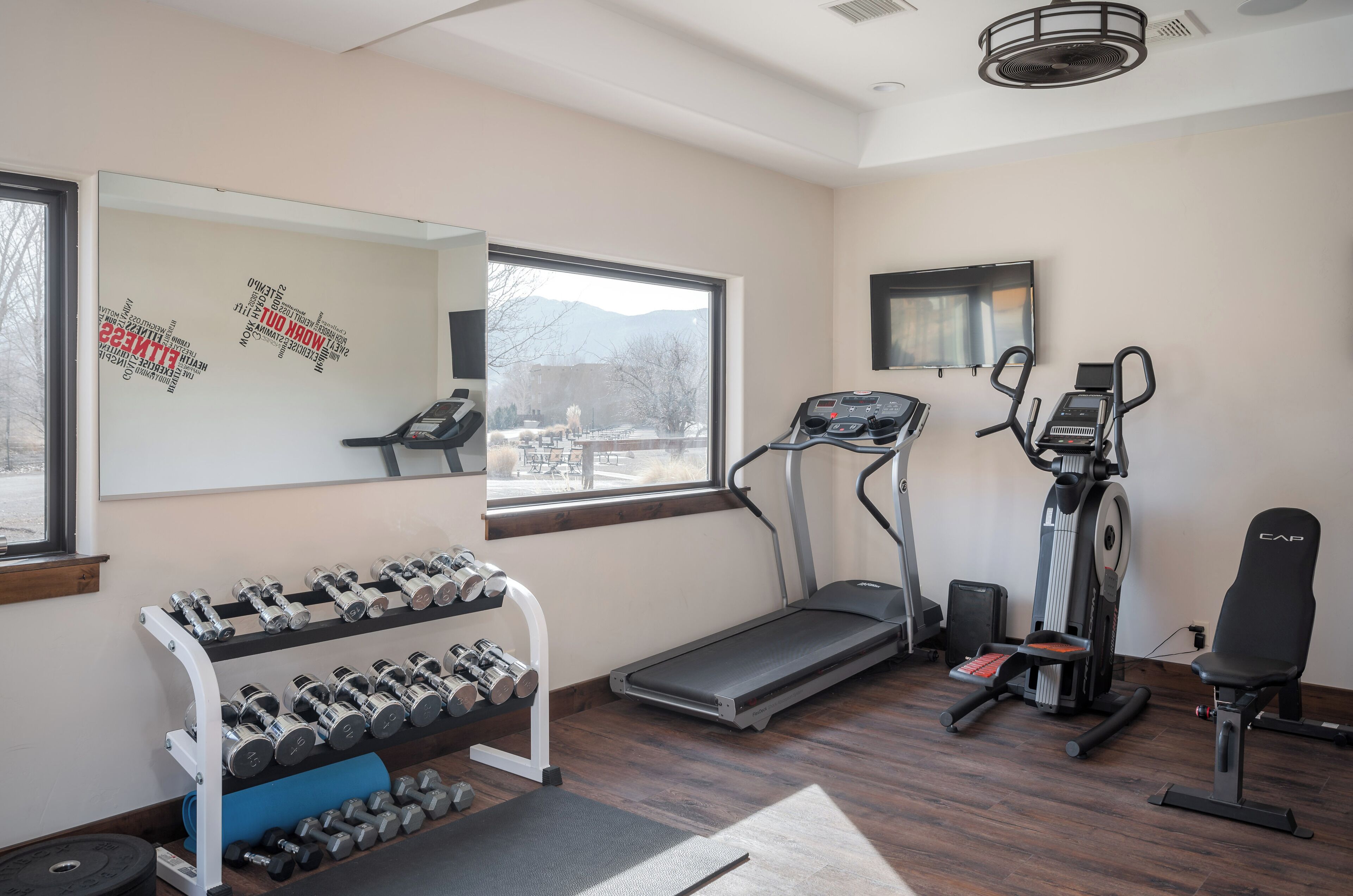 A gym with treadmills, elliptical machines, and a rack of dumbbells.