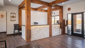 A reception area with a stone counter, wooden beams, a chair, and a door leading outside. - Village Camp Moab (Moab)