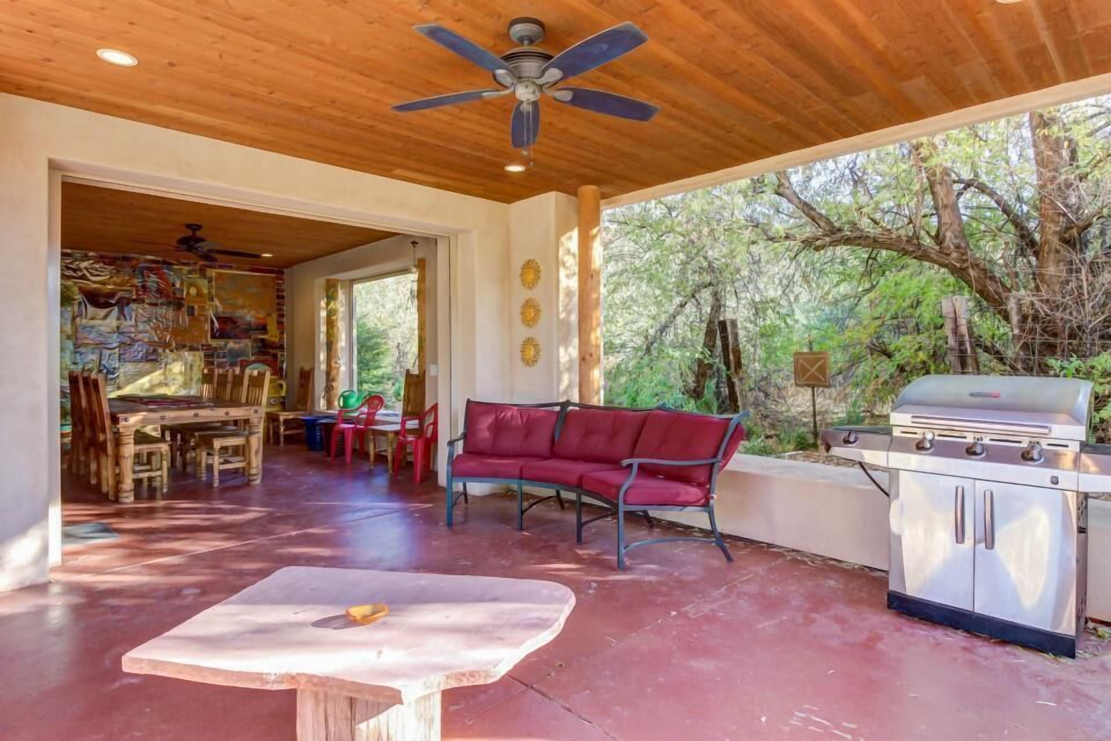 An outdoor patio with a red sofa, a barbecue grill, and a ceiling fan.
