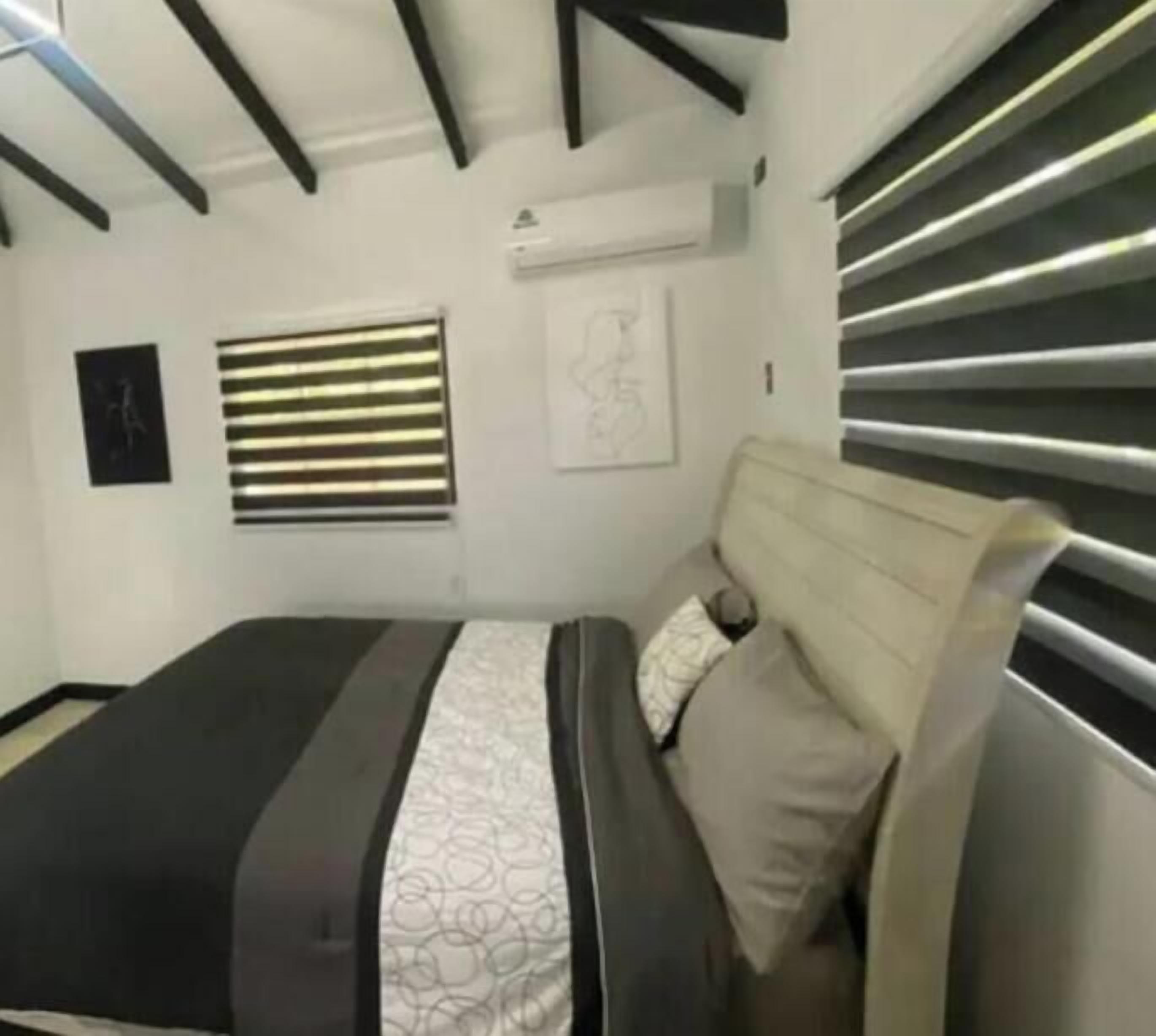 Une chambre moderne avec un lit, une tête de lit, un climatiseur fixé au mur et une fenêtre avec des stores.