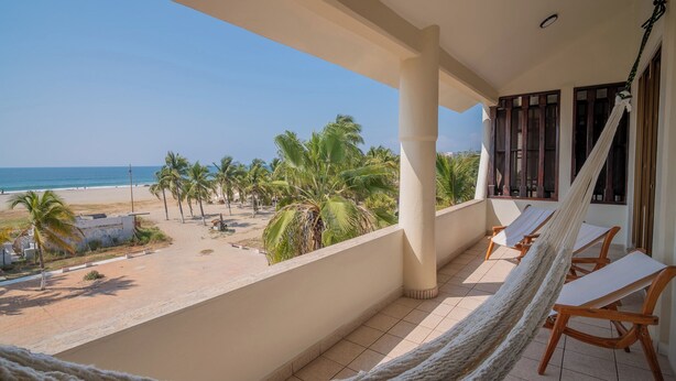 A balcony with a hammock, wooden chairs, and a view of the beach and palm trees. - Pacífico Surf  (Puerto Escondido)