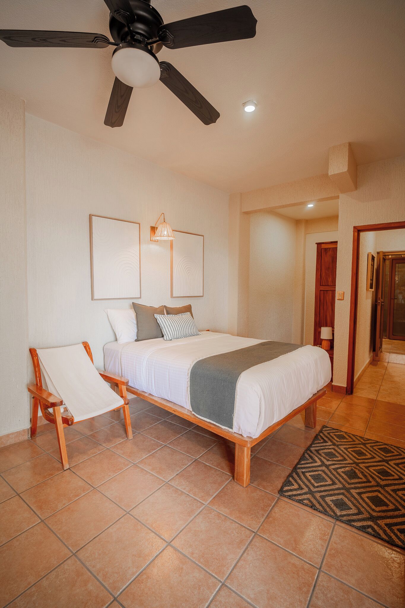 A bedroom with a bed, ceiling fan, and a door leading to another room.