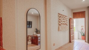 A hallway with a tiled floor, a round rug, a mirror, and a wall-mounted light fixture. - Pacífico Surf  (Puerto Escondido)