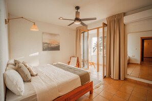 A bedroom with a bed, a ceiling fan, a painting on the wall, and a view through a glass door. - Pacífico Surf  (Puerto Escondido)