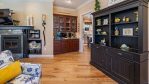 Un salón con chimenea, un sofá y una zona de cocina con armarios de madera y un mueble bajo de madera con adornos.