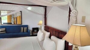 A bedroom with a canopy bed, a blue sofa in the background, and a lamp on the bedside table.
