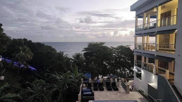 A hotel with a balcony overlooking the sea, surrounded by lush greenery.