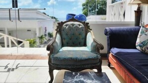 A room with a blue armchair, a dark blue sofa, and a marble coffee table. There is a white railing and a view of a building outside.
